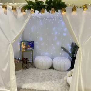 A cozy Ramadan tent decorated with white fabric, string lights, greenery, and golden lanterns.