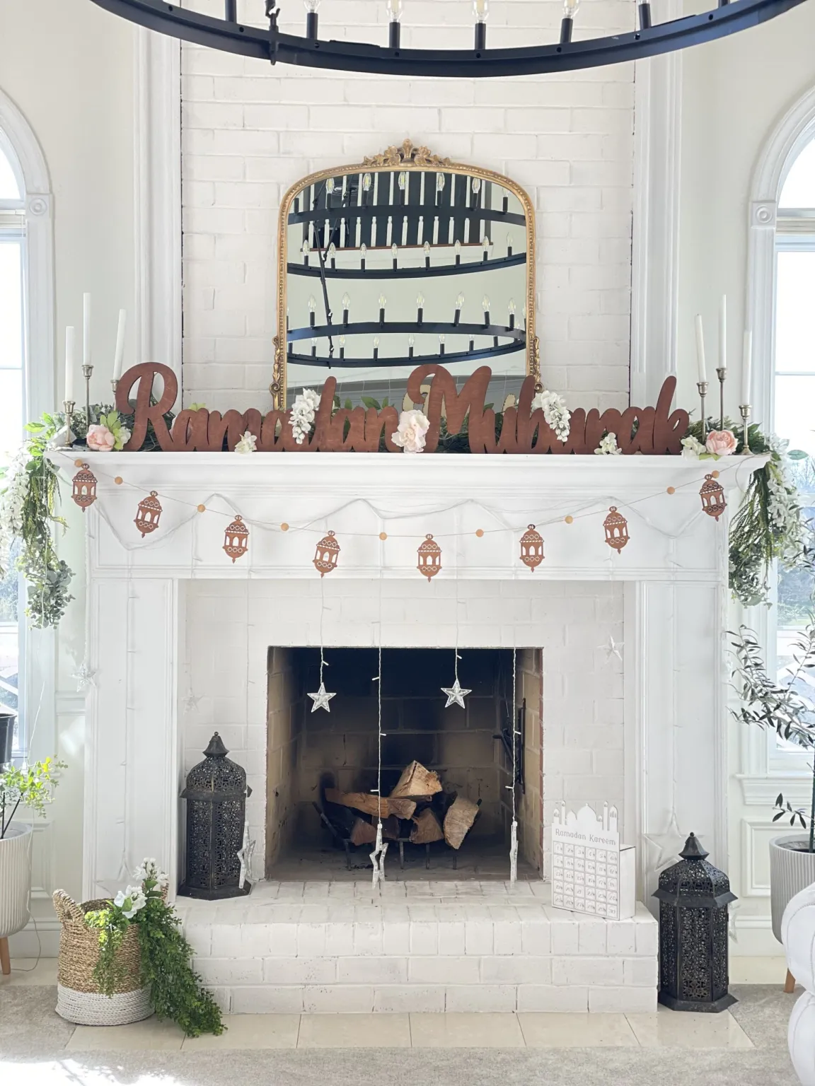 A white brick fireplace decorated for Ramadan with wooden 'Ramadan Mubarak' lettering, a lantern garland, hanging stars, and decorative lanterns.