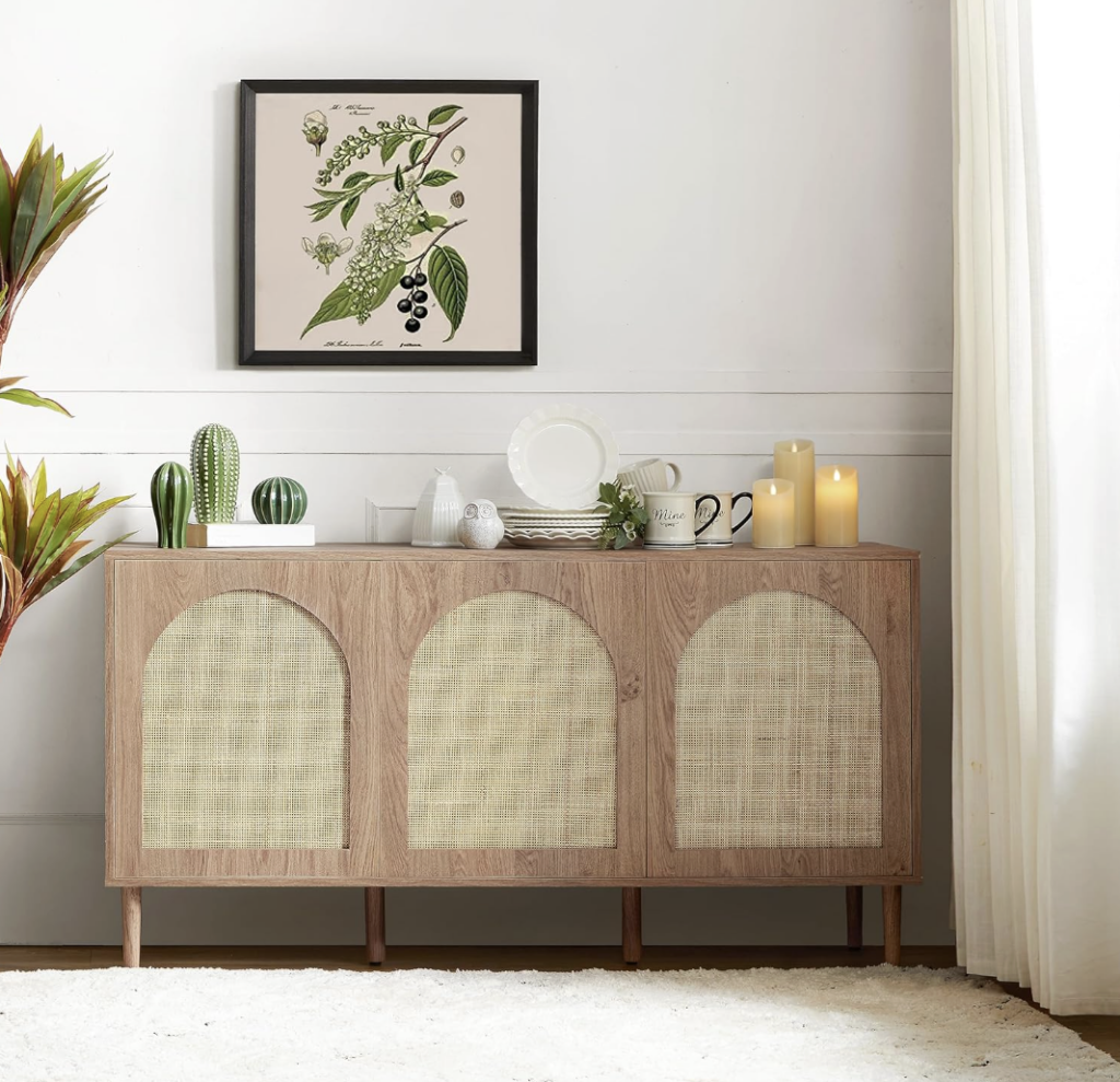 A light oak wood sideboard with three arched cane-paneled doors, decorated with various items including decorative cacti, plates, mugs, and candles.