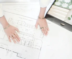 Hands of a person wearing jewelry and a white shirt on top of architectural blueprints.