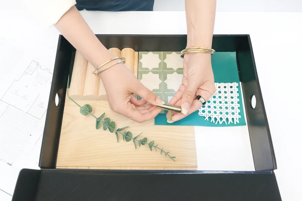 A person's hands are selecting a brass cabinet pull from a tray of interior design samples.